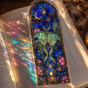 Può includere: Un segnalibro rettangolare con parte superiore arrotondata e design in stile vetrata. L'illustrazione mostra una grande falena verde, una lanterna accesa, una luna crescente e fiori rosa su uno sfondo blu intenso con dettagli dorati.