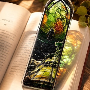 May include: A rectangular phone case with a stained glass design featuring an astronaut, green and orange foliage, and a futuristic structure. The case is resting on an open book with the text "CHAPTER XV".