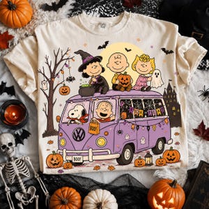 May include: A cream-colored t-shirt featuring a graphic of Peanuts characters in a purple van. The design includes Lucy as a witch, Charlie Brown with a pumpkin, and Sally with a ghost sheet. Snoopy drives the van, which is decorated with Halloween bunting, spiderwebs, and the text 'TRICK OR TREAT' and 'BOO'.