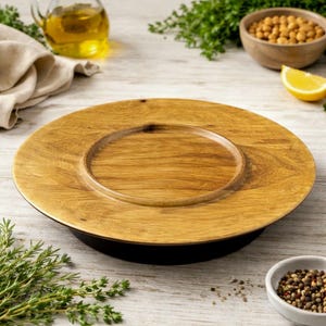 May include: A round wooden serving platter with a raised center, showcasing a natural wood grain. The platter sits on a black base. The image also includes a bowl of chickpeas, a lemon wedge, and a small bowl of peppercorns.