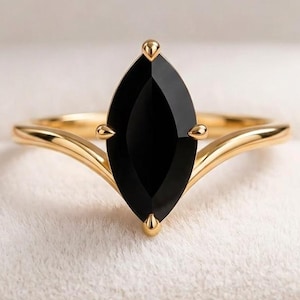 Può includere: Un anello in oro con una singola pietra preziosa nera taglio marquise montata su griffe. La fascia presenta un design a gambo diviso che si assottiglia verso la pietra centrale, conferendo un aspetto elegante e raffinato a questo gioiello.