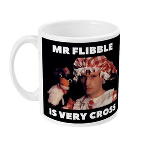 May include: White ceramic mug featuring a black graphic with the text "MR FLIBBLE IS VERY CROSS". The graphic includes an image of a person and a puppet. The mug has a white handle.