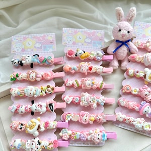 Puede incluir: Una colección de pinzas para el pelo rosas con varios personajes de dibujos animados en miniatura, alimentos y formas coloridas unidas a clips de metal rosa. Las pinzas se muestran en tres tarjetas de cartón rosa etiquetadas Puppy Room.