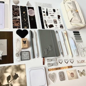 May include: An assortment of stationery items, including a gray notebook, pens, stickers, bookmarks, and a pencil case. Decorative elements include heart-shaped embellishments, bow-shaped paper clips, and a metal bookmark with the text "Do not fear For I am with you."