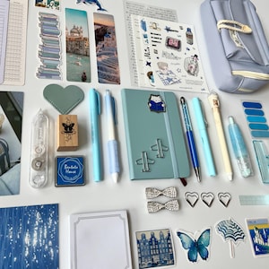 May include: An assortment of stationery items in shades of blue and white, including pens, a notebook, stickers, and a pencil case. Decorative elements include heart-shaped paper clips, butterfly stickers, and a stamp with a butterfly design.