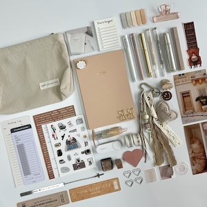 Könnte beinhalten: Eine Auswahl an Schreibwaren und Accessoires, darunter ein beiges Cord-Etui, ein Notizbuch, Stifte, Aufkleber und ein Schlüsselanhänger. Die Artikel sind auf einer weißen Oberfläche angeordnet, mit einer neutralen Farbpalette.