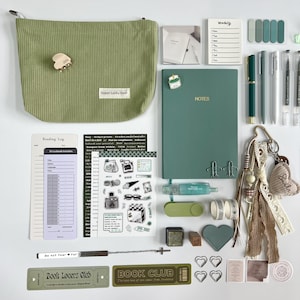 K&ouml;nnte beinhalten: Eine Auswahl an Schreibwaren in Gr&uuml;n- und Wei&szlig;t&ouml;nen, darunter eine Cord-Beuteltasche, ein Notizbuch, Stifte, Aufkleber und ein Leseprotokoll. Die Tasche hat einen B&auml;renkrallen-Anh&auml;nger und den Text "Super Lucky Deer". Ein Notizbuch mit der Aufschrift "NOTES".