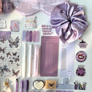 May include: A collection of purple and lavender stationery and accessories, including a sleep mask, scrunchie, pens, stickers, washi tape, and a reading list. The items are arranged on a white surface, creating a visually appealing aesthetic.