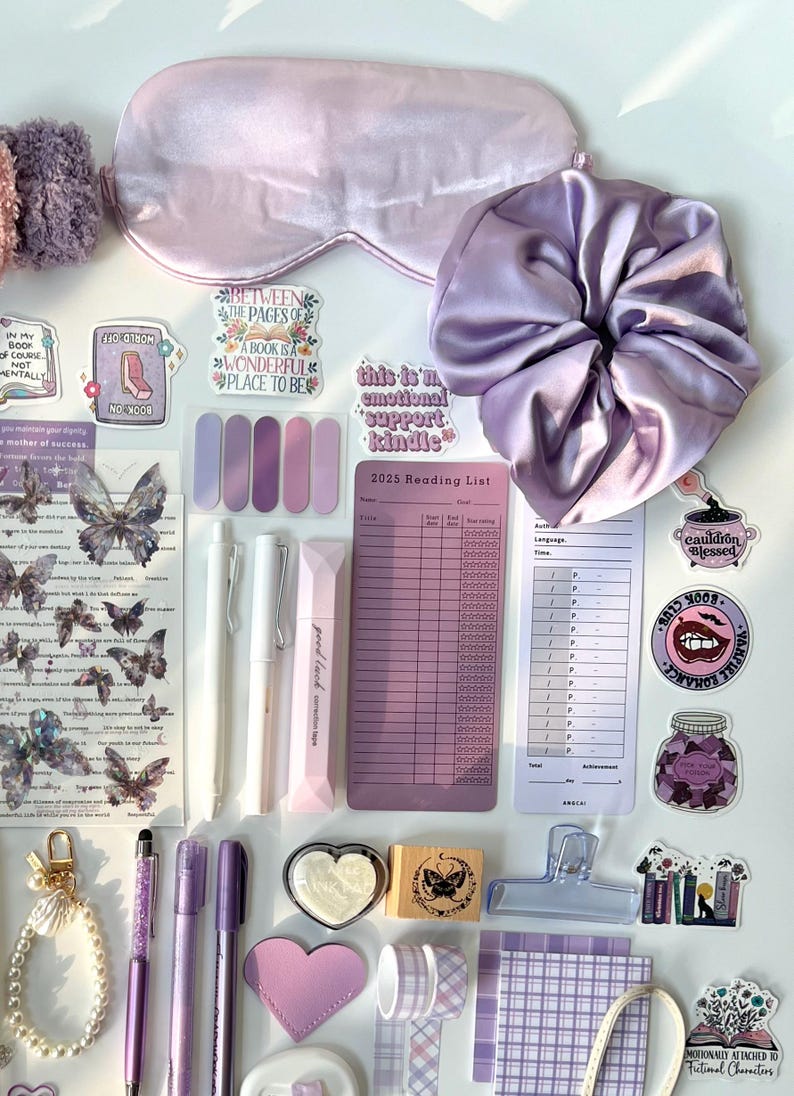 May include: A collection of purple and lavender stationery and accessories, including a sleep mask, scrunchie, pens, stickers, washi tape, and a reading list. The items are arranged on a white surface, creating a visually appealing aesthetic.
