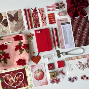 Puede incluir: Un surtido de artículos de papelería y accesorios en tonos rojos, rosas y blancos, que incluyen un diario, bolígrafos, pegatinas y una bolsa decorativa con bordados florales rojos. También hay tarjetas y adornos con temas de mariposas y flores.