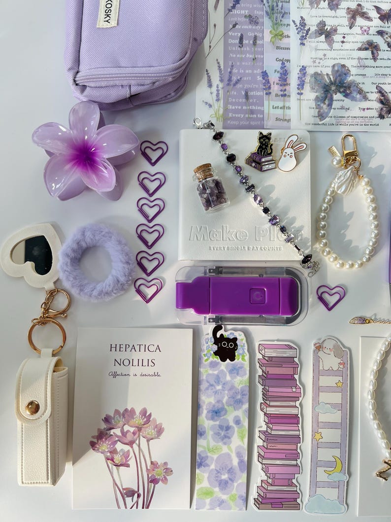 May include: A collection of purple and white stationery items, including a small bag, flower-shaped clip, heart-shaped paper clips, a bracelet, a notebook, and stickers. The notebook reads "Make Plans Every Single Day Counts".