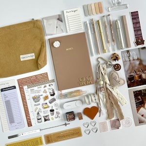 Puede incluir: Un surtido de artículos de papelería en tonos neutros, que incluyen una bolsa de pana, un cuaderno, bolígrafos, pegatinas y accesorios decorativos. Los artículos son de color beige, marrón y dorado. El texto "Super Lucky Deer" y "NOTES" es visible.