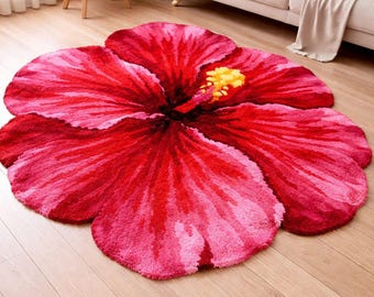 May include: A large, round rug shaped like a red and pink hibiscus flower. The rug has a detailed design with a yellow center and is placed on a light-colored wooden floor. The rug adds a vibrant floral accent to the room.