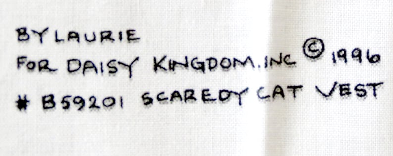 May include: Text on a white fabric reads "BY LAURIE FOR DAISY KINGDOM.INC &copy; 1996 # B59201 SCAREDY CAT VEST". The text is in black, handwritten-style lettering.