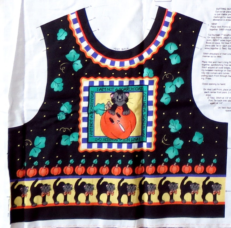 May include: Black vest fabric with a Halloween theme. The design includes a central square with a cat on a pumpkin and the text "I AM NOT A SCARDY CAT". The vest also features pumpkins, black cats, and green leaves.