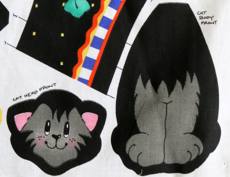 May include: A fabric panel featuring cat-themed designs. The panel includes a cat head with pink ears and a smiling face, and a cat body front. The background has black and white geometric shapes with colorful accents. Text includes "CAT HEAD FRONT" and "CAT BODY FRONT".