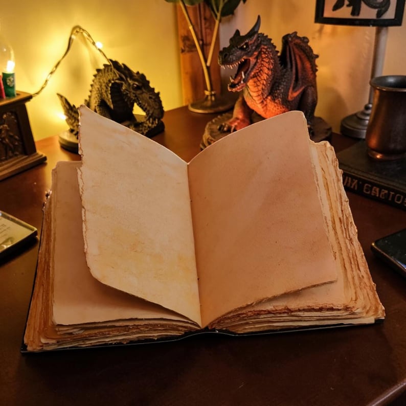 May include: An open book with thick, cream-colored pages featuring rough, deckled edges. The paper has a textured, aged appearance with visible fibers. The book is positioned flat, displaying two blank pages spread wide for writing or sketching.
