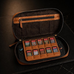 Könnte beinhalten: Geöffnete braune Leder-Tragetasche mit Reißverschluss, die eine schwarze Spielkonsole und Spielkassetten enthält. Die Tasche hat ein braunes Innenfutter mit einer Reißverschlusstasche und einem Halter für die Spielkassetten.