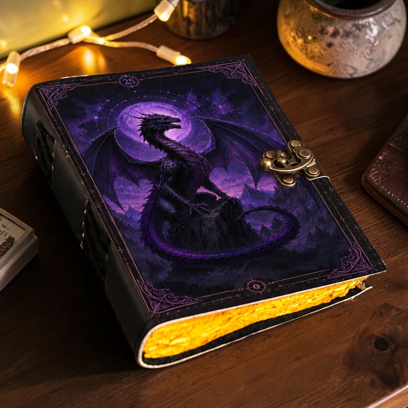 May include: A rectangular journal featuring a dark purple and black cover with a dragon illustration set against a full moon. The book includes a metallic brass-colored latch closure and thick, textured pages with a vibrant yellow-gold edge finish.