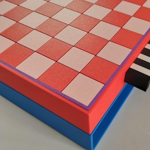 K&ouml;nnte beinhalten: Ein geometrisches Schachbrett mit einem rot, rosa und wei&szlig; karierten Muster. Das Brett ist rot umrandet, mit einem lila Rand, und steht auf einer blauen Basis. Eine schwarz-wei&szlig;e Schublade ist sichtbar.