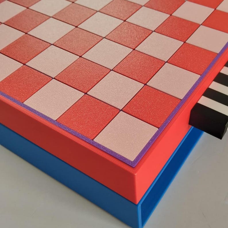 K&ouml;nnte beinhalten: Ein geometrisches Schachbrett mit einem rot, rosa und wei&szlig; karierten Muster. Das Brett ist rot umrandet, mit einem lila Rand, und steht auf einer blauen Basis. Eine schwarz-wei&szlig;e Schublade ist sichtbar.