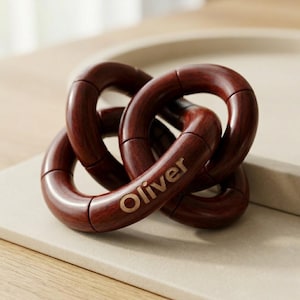 May include: A decorative wooden knot sculpture in a rich, dark brown finish. The interlocking rings are smooth and polished, with the name "Oliver" in gold lettering. A modern home decor accent.