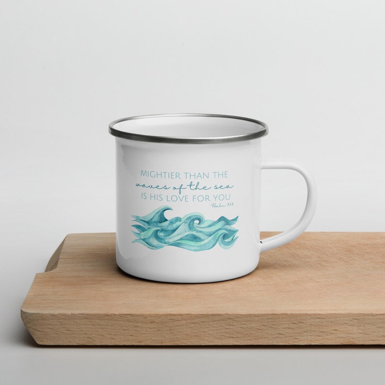 May include: White enamel mug featuring a blue watercolour design of ocean waves. The mug has a silver rim and handle. The text on the mug reads "Mightier than the waves of the sea is his love for you. Psalm 93:4".