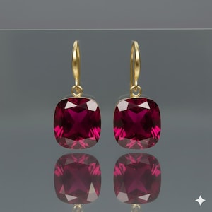 May include: A pair of gold-coloured drop earrings. Each earring features a large, square-cut, deep red gemstone. The gemstones are faceted, reflecting light. The earrings have a simple, elegant design, suitable for various occasions.