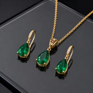 Può includere: Un set di gioielli in oro composto da una collana e due orecchini abbinati. Ogni pezzo presenta una gemma verde a forma di pera incastonata in oro con piccole pietre bianche d'accento sui ganci e sulla montatura del pendente.
