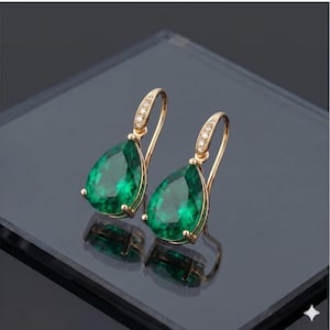 May include: A pair of gold-colored drop earrings with large, pear-shaped, emerald-green gemstones. The earrings have a delicate design, with small clear stones set along the top curve of the hook.