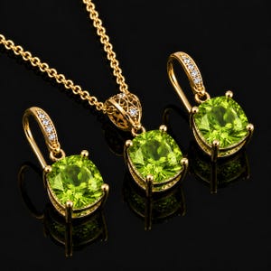 May include: A gold jewellery set consisting of a pendant necklace and two matching earrings. Each piece features a large, cushion-cut, lime green gemstone held in a four-prong setting, accented by small clear stones on the gold metal hooks.