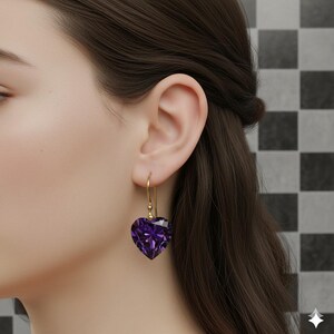 May include: A pair of heart-shaped amethyst earrings. The earrings feature a faceted, deep purple gemstone suspended from a delicate gold-colored hook. The heart-shaped gems are cut to catch the light, creating a sparkling effect. The earrings are shown against a neutral background.