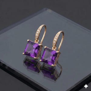 Könnte beinhalten: Ein Paar goldfarbene Ohrringe mit quadratischen, tiefvioletten Edelsteinen. Die Ohrringe haben ein Bügeldesign mit einer Reihe kleiner, klarer Steine auf der Oberseite des Hakens. Die Ohrringe werden auf einer reflektierenden Oberfläche präsentiert.