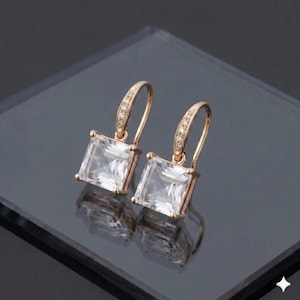 May include: A pair of gold-coloured drop earrings featuring square, clear, faceted stones. The earrings have a lever back closure and are embellished with small, sparkling crystals along the top of the hook.