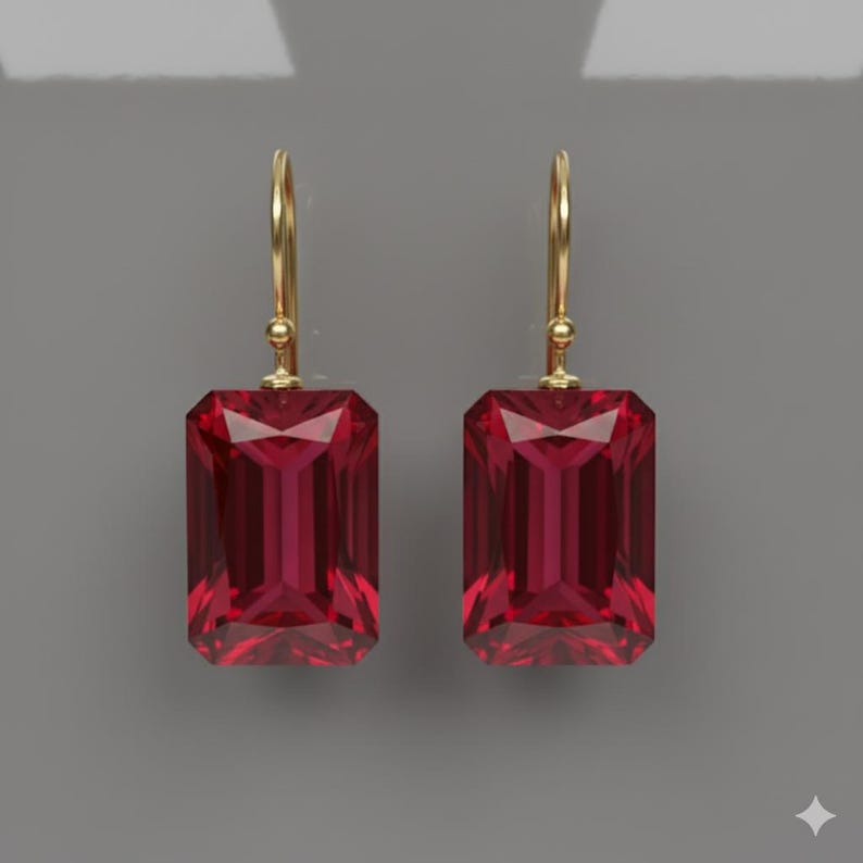 K&ouml;nnte beinhalten: Ein Paar goldfarbene Ohrh&auml;nger mit gro&szlig;en, rechteckigen, facettierten, rubinroten Edelsteinen. Die Ohrringe haben ein schlichtes, elegantes Design mit Hakenverschluss. Die Edelsteine sind tiefrot.