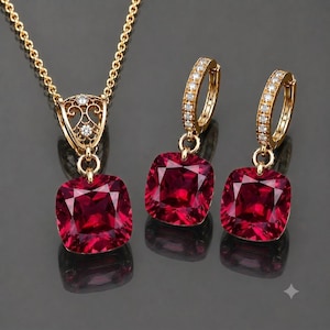 Könnte beinhalten: Ein goldfarbenes Schmuckset bestehend aus einer Halskette und zwei Creolen. Jedes Stück ist mit einem quadratisch geschliffenen, tiefroten Edelstein besetzt. Der Anhänger der Kette hat eine verzierte Filigranöse mit kleinen, klaren Steinen.
