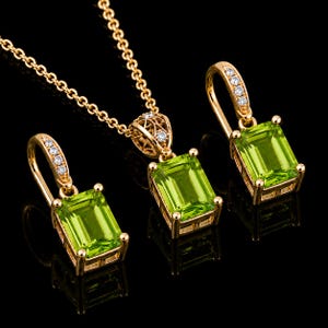 May include: A gold jewelry set consisting of a necklace and two earrings. Each piece features a rectangular emerald-cut lime green gemstone set in gold, with small clear accent stones embedded along the gold bail and pendant settings.