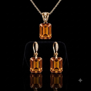 May include: A gold jewelry set consisting of a pendant necklace and matching drop earrings. Each piece features a large, emerald-cut orange citrine gemstone set in gold, with small clear accent stones on the bail and earring hooks.