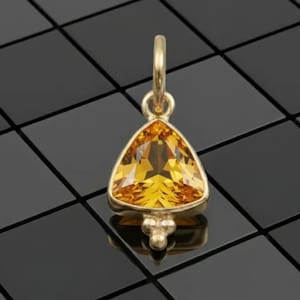 May include: A gold pendant featuring a triangular, faceted, yellow gemstone. The pendant has a small loop for a chain and three small decorative spheres. The gemstone is a vibrant, warm yellow colour.