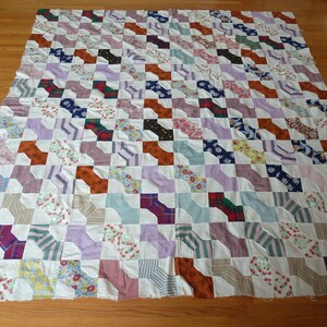 May include: A patchwork quilt with a pattern of brown, purple, blue, and white bow ties. The quilt is made of various fabrics with floral, plaid, and striped patterns.