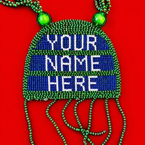 May include: A beaded necklace featuring a semi-circular pendant with the text YOUR NAME HERE in white beads against a blue background, framed by green and brown beads. The piece includes two large green beads and dangling beaded fringe strands.
