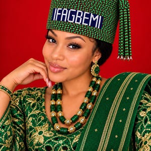 Pode incluir: Um gorro de contas verdes com borla e o texto IFAGBEMI em letras brancas, combinado com um colar, brincos e pulseira a condizer em verde e ouro. O conjunto apresenta um trabalho intrincado de contas e detalhes dourados numa peça verde.