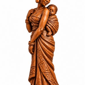 Puede incluir: Una escultura de madera marrón que representa a una persona con un pañuelo en la cabeza y una prenda larga con patrones geométricos, cargando a un niño pequeño en la espalda con un envoltorio. La figura tiene detalles tallados y base redonda.