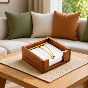以下が含まれることがあります： 温かみのあるブラウン仕上げの正方形の木製ナプキンホルダー。ゴールドトーンの金属製ウェイトアームが付いており、先端の球体で白い正方形のナプキンをオープンフレーム内にしっかりと固定します。