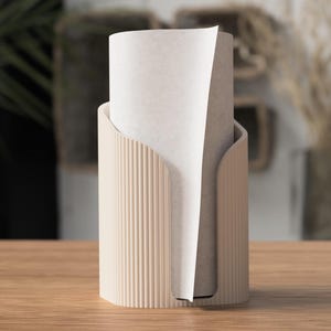 May include: A beige paper towel holder with a vertical ribbed design. The holder has a curved opening to dispense paper towels. A roll of white paper towels is inside the holder. The holder is on a wooden surface.
