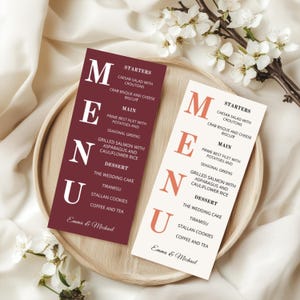 May include: Two wedding menus are displayed on a wooden tray, one in burgundy and the other in cream. The menus list starters, main courses, and desserts. The burgundy menu has white text, while the cream menu has orange text. Both menus are personalized with the names "Emma & Michael".