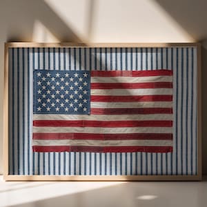 Könnte beinhalten: Ein gerahmtes Textilkunstwerk mit einer amerikanischen Flagge aus Stoff, die ein blaues Feld mit weißen Sternen sowie rote und weiße Streifen zeigt, platziert auf einem Hintergrund mit blauen und weißen vertikalen Streifen in einem hellen Holzrahmen.