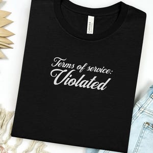 Puede incluir: Camiseta negra con el texto blanco "Terms of service: Violated". La camiseta tiene cuello redondo y está hecha de un material suave. La palabra "Black" está impresa en la parte inferior de la imagen.