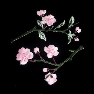 Puede incluir: Dos ramas florales bordadas con flores rosas y hojas verdes sobre un fondo negro. Las flores tienen múltiples pétalos y están en varias etapas de floración. Las ramas son de color verde oscuro.