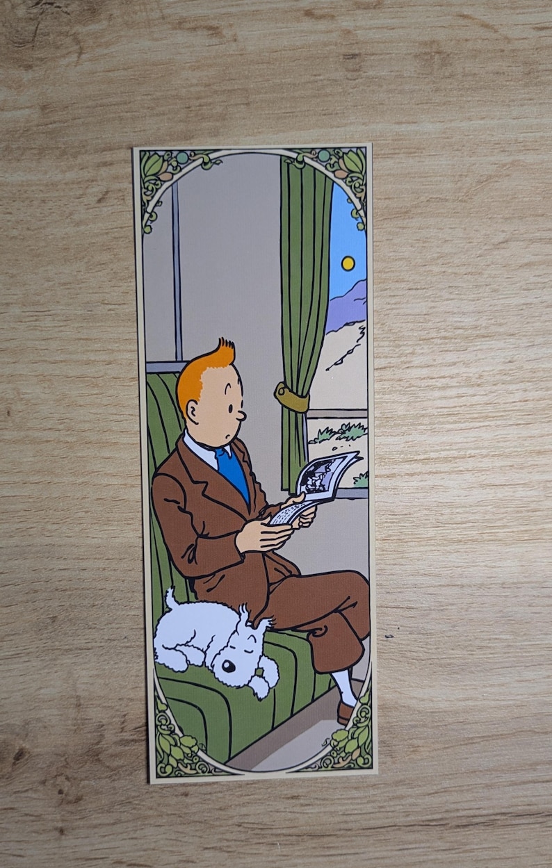 May include: A rectangular bookmark featuring a colorful illustration of a man with orange hair wearing a brown suit and blue tie, sitting on a green seat while reading a book. A small white dog is curled up asleep on the seat beside him.